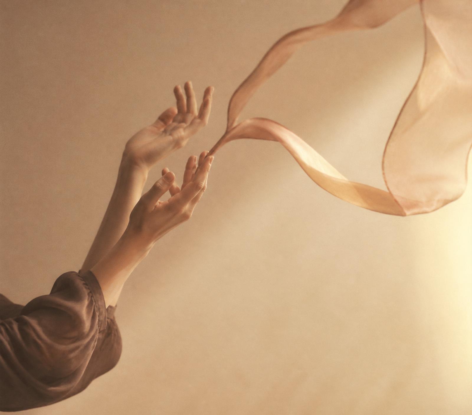 Hands releasing a silk ribbon in warm light